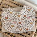 Handmade baby bib with illustrated chickens and scattered florals in earthy tones on a neutral background; backed with absorbent terry towelling, ideal for newborns and everyday use.