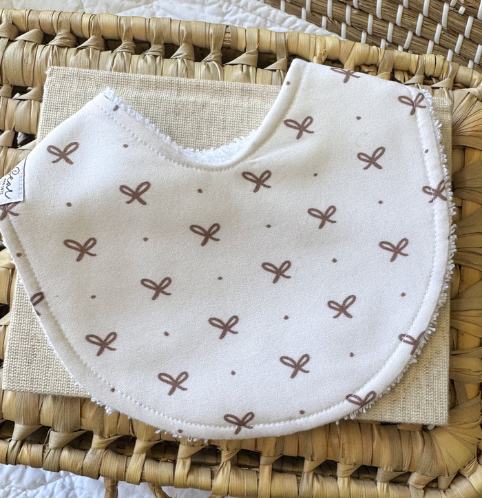Baby girl handmade bib. Cotton fabric is white with mini brown bows and spots scattered across it.