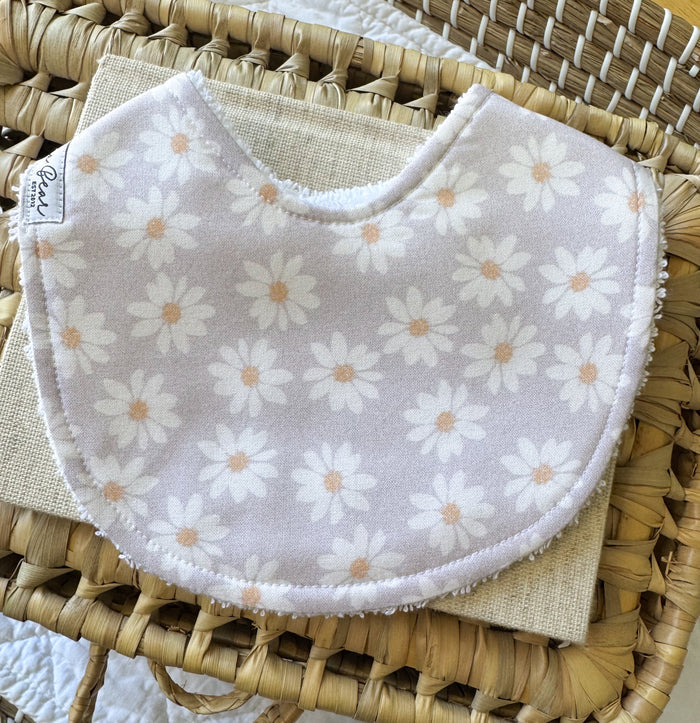 Baby girl bib in a pale purple background , with white daisies and orange centres.