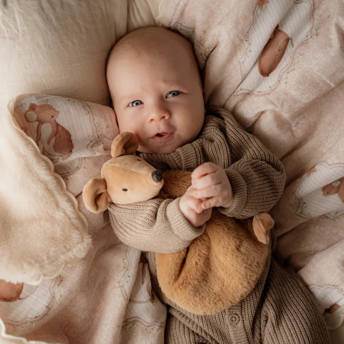 Baby holding a teddy mouse in a cozy, patterned crib