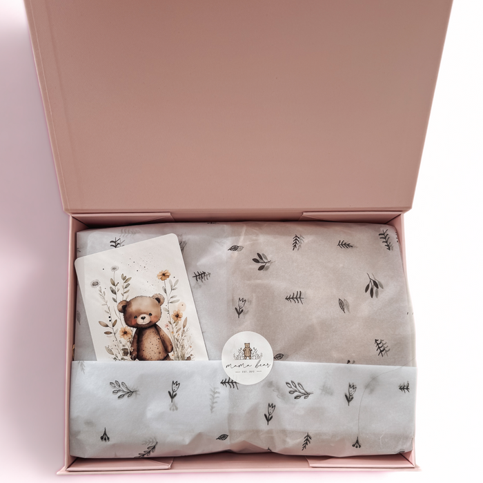 Inside view of pastel pink baby gift box with tissue wrap, Mama Bear sticker seal, and illustrated teddy bear card — a sweet and thoughtful baby girl gift or newborn keepsake.