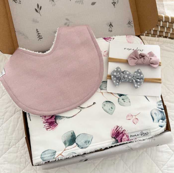 A baby girl gift set featuring a dusty pink bib, a white blossom floral burp cloth, and two matching hair bows in a solid Dusty pink fabric and a grey and white spot fabric.