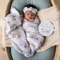 Newborn baby wrapped in a swaddle blanket with ducks on it and a 'I'm here' sign in a wicker basket.