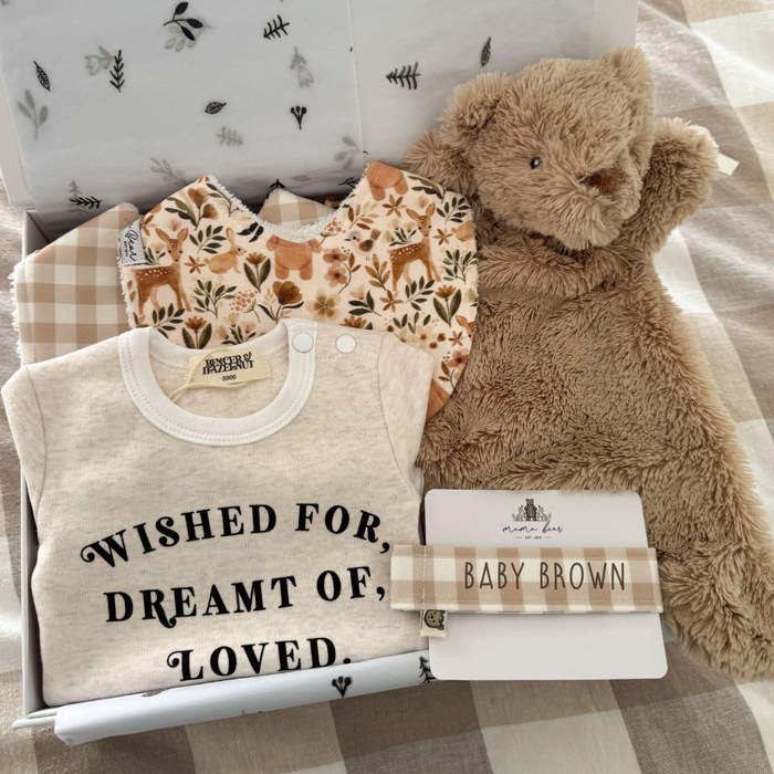 Gender neutral baby shower luxury gift hamper featuring a snuggly brown teddy bear comforter, a beige bodysuit with black text saying 'Wished for, dreamt of, loved. A beige gingham bib, a bib with illustrations of woodland animals and florals such as deer, rabbit and bears and a coordinating dummy clip in beige gingham with 'baby brown' personalised on it.