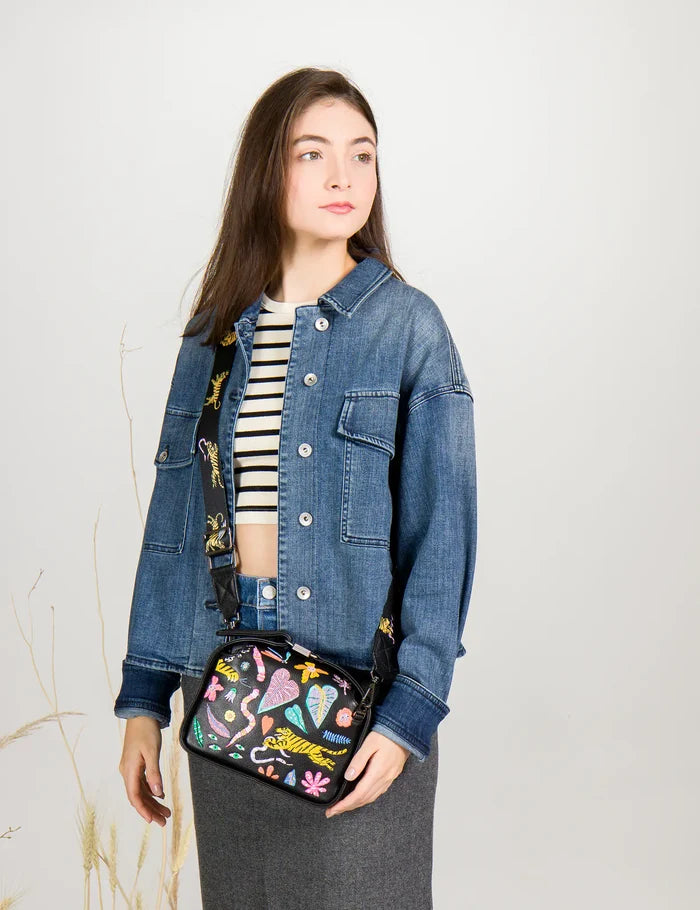 Woman wearing a denim jacket holding a colorful handbag against a plain background
