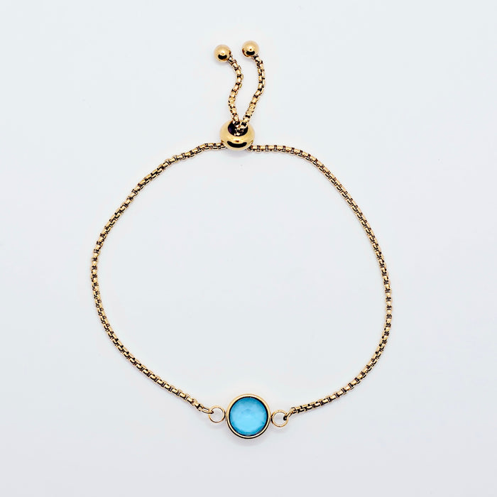 Gold penis noose bracelet with a blue gemstone on a light gray background