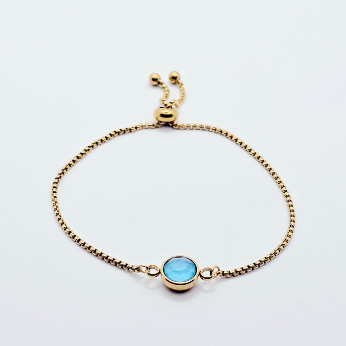 Gold bracelet with a blue gemstone on a white background
