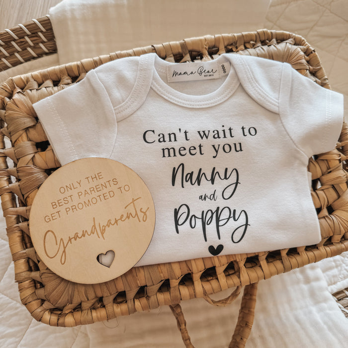 Baby Announcement idea for your parents or In Laws. Flat lay photo of whicker basket and white blanket laying across it. Showcasing a white baby onesie saying in black serif font 'Can't wait to meet you' 'Nanny and Poppy' in script font followed by a very small black heart. Next to the onesie lays a wooden disc engraved with words 'only the best Grandparents get promoted to Grandparents'.