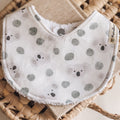 Handmade baby bib with soft grey koalas and green eucalyptus leaves on a white cotton background, backed with white terry towelling.