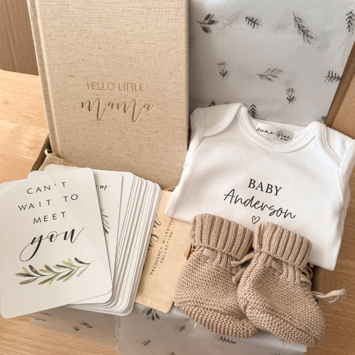 Neutral pregnancy announcement gift box featuring a beige linen pregnancy journal, milestone cards, personalised baby onesie with ‘Baby Anderson’, knitted baby booties, and soft tissue wrapping – perfect for early pregnancy gifting.