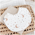 Handmade baby bib with a soft moon and star print in earthy browns and beige on a white base. Bib is backed with beige terry towelling and displayed on a woven basket.