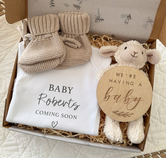 Baby announcement gift set with booties, blanket, and plush lamb toy in a box.
