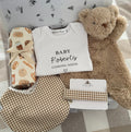 Baby shower gift set with personalsied baby onesie 'Baby Roberts coming soon', soft brown teddy bear comforter, brown gingham check baby bib & matching dummy clip and a cream swaddle with cute illustrations of bakery foods such as danishes and bread. Packaged inside a white gift box.