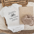 White onesie with black text ' We're going to need another bike *picture of bike* Baby Roberts Pedalling in *due date*
