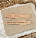 Two personalised wooden pregnancy test sticks are displayed. The top test is engraved with a heart and 'Pregnant / Not Pregnant' options with  '+' meaning pregnant. And the bottom test is customised with 'Baby McDonald - due March 2027'.