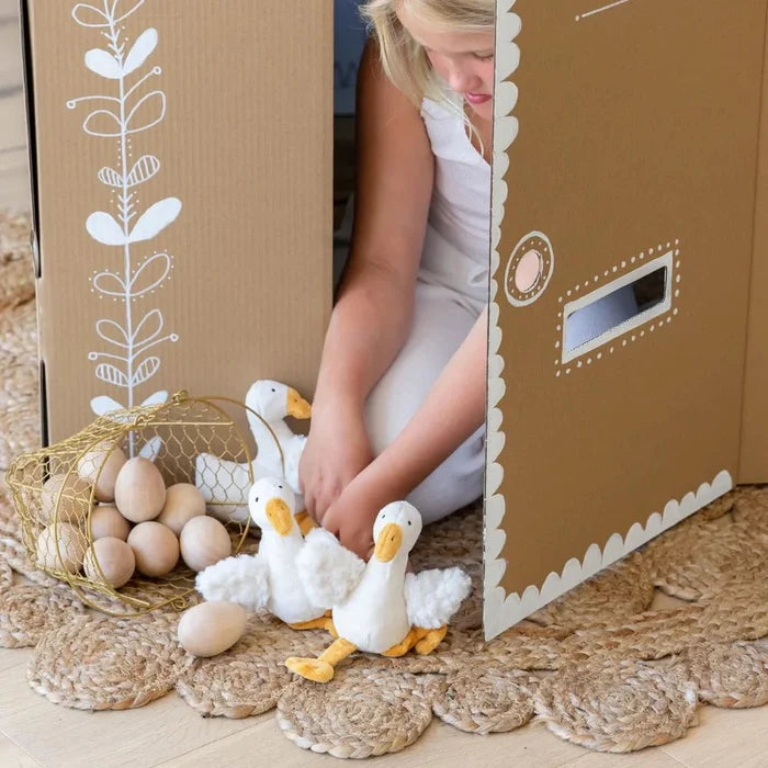 Child playing with toy ducks and eggs near a cardboard box with decorative elements.